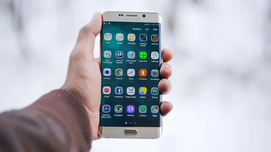 A hand holding a Samsung smartphone showing its home screen