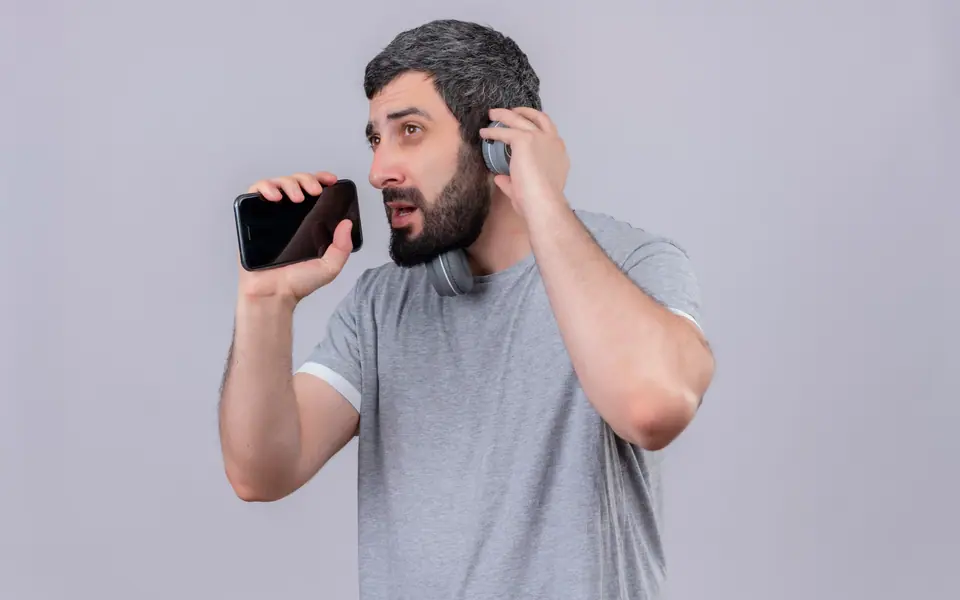 A man holding a phone to speak, with headphones around his neck