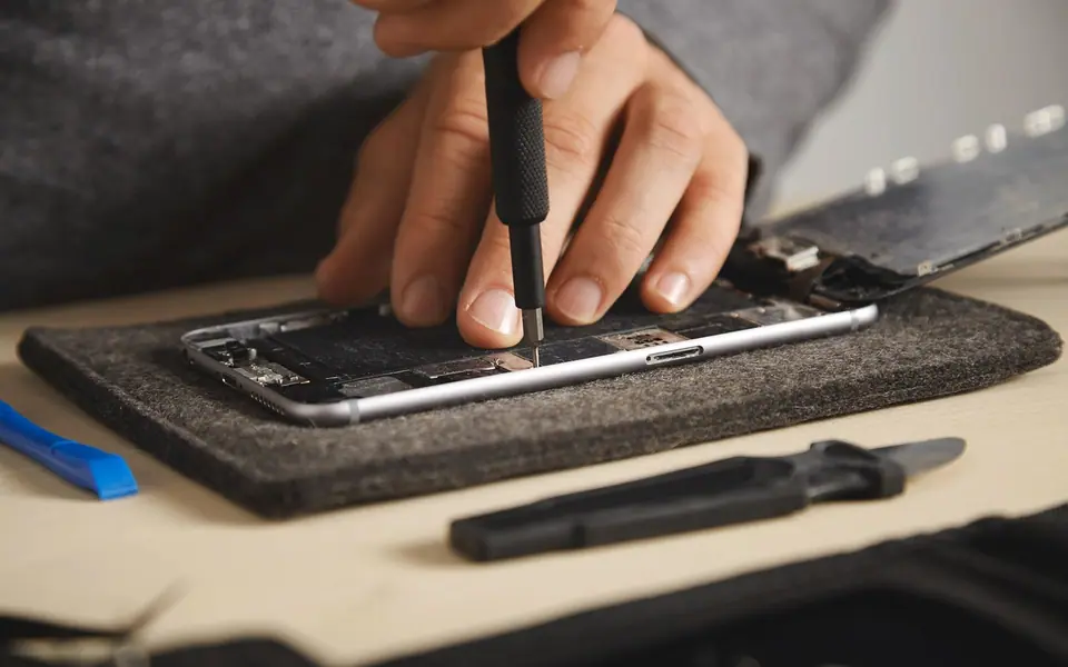 Hands using a small screwdriver to repair a disassembled phone