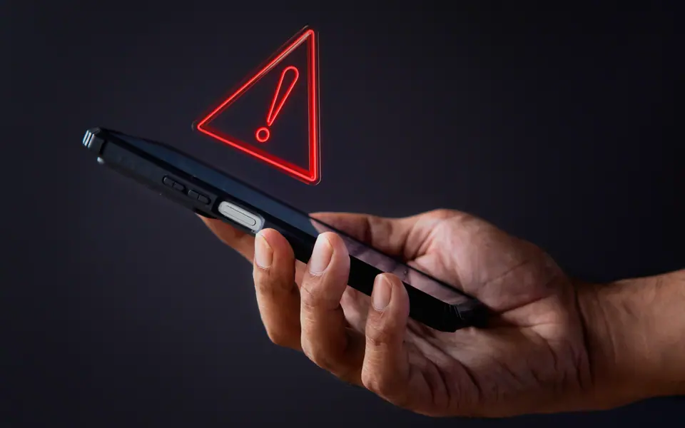 A hand holding a phone showing a software warning icon